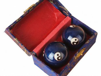 Dwie chińskie kule zdrowia z symbolami yin-yang w ozdobnym pudełku z czerwonym wnętrzem.