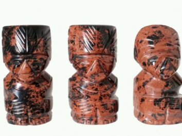 Trzy rzeźbione figurki z czarno-czerwonego kamienia ustawione obok siebie na jasnym tle.