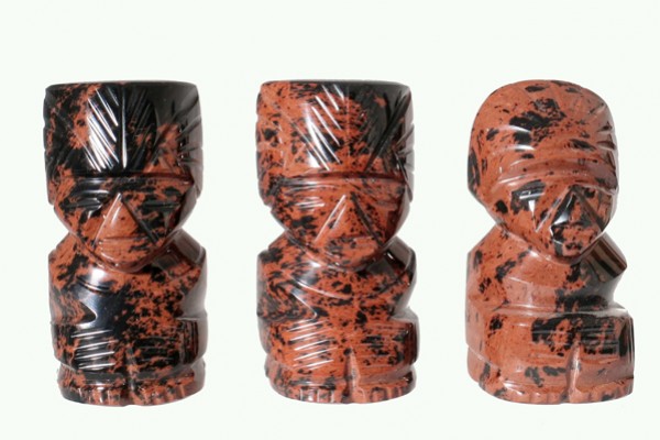 Trzy rzeźbione figurki z czarno-czerwonego kamienia ustawione obok siebie na jasnym tle.