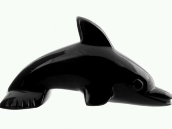 Czarna, błyszcząca figurka delfina ustawiona bokiem na jasnym tle.