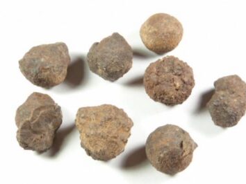 Hematyt - kamień naturalny, surowy, nieszlifowany. Osiem kamieni o nieregularnym kształcie leży na białym tle.