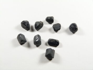 Czarny turmalin, kamień silnej ochrony energetycznej w postaci surowych bryłek na jasnym tle.