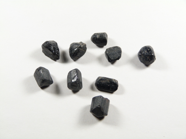 Czarny turmalin, kamień silnej ochrony energetycznej w postaci surowych bryłek na jasnym tle.
