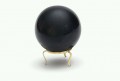 Czarna kula ustawiona na małej, złotej podstawce na jasnym tle.