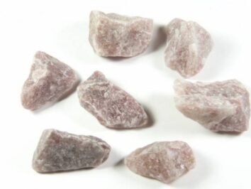 Siedem surowych, różowych kamieni leży na białym tle.