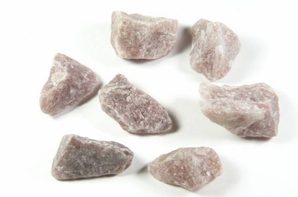 Siedem surowych, różowych kamieni leży na białym tle.