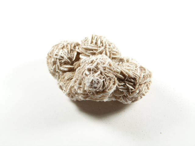 Kamień zwany różą pustyni na białym tle, skupisko kryształów przypominających kwiaty.