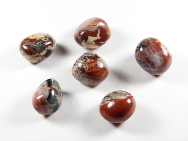 Jaspis makowy kamień optymizmu w odcieniach czerwieni, beżu i czerni – kamień radości i wewnętrznej równowagi. Sześć wypolerowanych kamieni jaspisu makowego leży na białym tle.