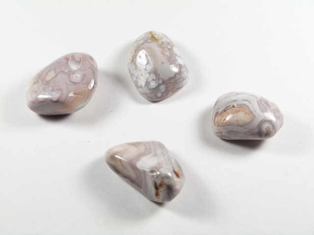 Agat różowy kamień gładzony w szaro-różowej barwie. Cztery polerowane kamienie agatowe leżą na białym tle.