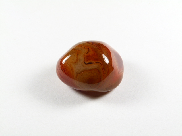 Agat z Madagaskaru kamień gładzony – widok z drugiej strony. Polerowany, brązowo-czerwony kamień leży na białym tle.