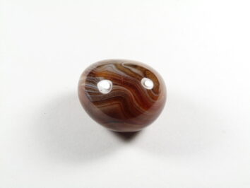 Agat kamień naturalny gładzony. Brązowy, wypolerowany kamień z wyraźnymi białymi paskami na białym tle.