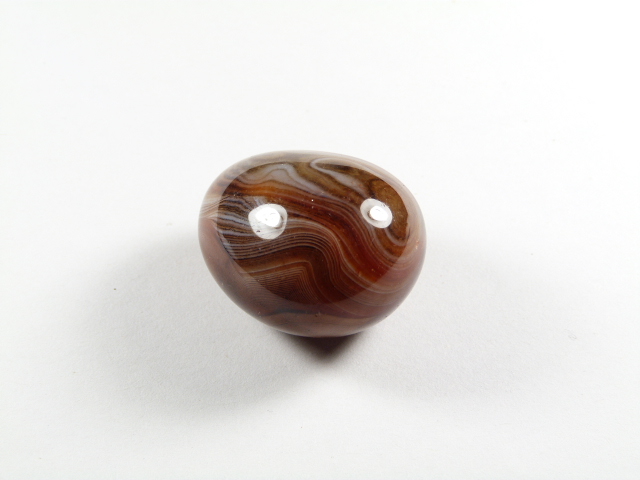 Agat kamień naturalny gładzony. Brązowy, wypolerowany kamień z wyraźnymi białymi paskami na białym tle.