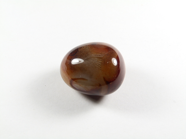 Agat kamień gładzony brązowy egzemplarz, Wypolerowany, brązowy kamień agat leży na białym tle.