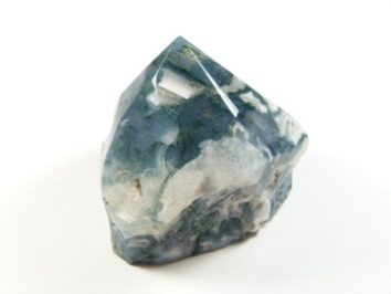 Agat mszysty zielony w szlifowanej formie z zielonymi, przypominającymi mech wzorami. Polerowany okaz agatu mszystego o zielono-białym zabarwieniu na białym tle.