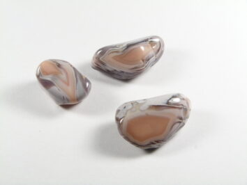Agat różowy kamień gładzony – przykładowe egzemplarze. Trzy wypolerowane agaty w odcieniach beżu i szarości na białym tle.