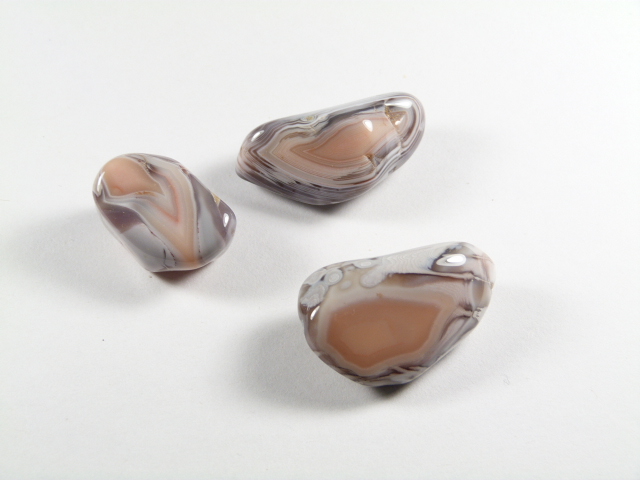 Agat różowy kamień gładzony – przykładowe egzemplarze. Trzy wypolerowane agaty w odcieniach beżu i szarości na białym tle.