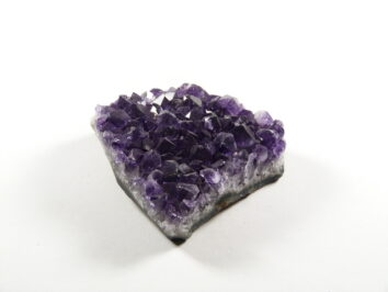 Ametyst kamień harmonii przedstawiony jako naturalna szczotka krystaliczna o intensywnym, fioletowym kolorze i połyskujących kryształkach. Fioletowy kryształ ametystu na białym tle.