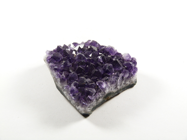 Ametyst kamień harmonii przedstawiony jako naturalna szczotka krystaliczna o intensywnym, fioletowym kolorze i połyskujących kryształkach. Fioletowy kryształ ametystu na białym tle.
