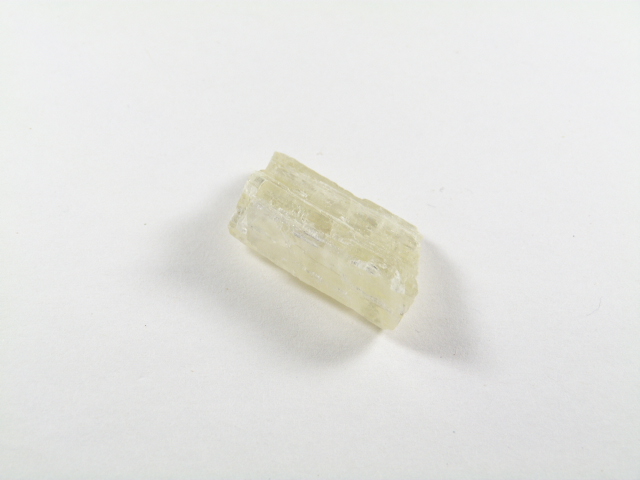 Hiddenit zielony naturalny surowy kryształ lekko przezroczysty. Przezroczysty kryształ minerału leży na białym tle.