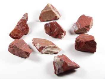 Jaspis czerwony kamień surowy – przykładowe egzemplarze. Osiem kawałków czerwonego jaspisu na białym tle.
