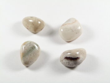 Sardoniks/ sardonyks - kamień gładzony, polerowany, szlifowany i bębnowany w formie otoczaka. Kamień sardoniks w formie naturalnych, gładzonych, jasnych kamyczków. Cztery gładkie, jasne kamienie leżące na białym tle.