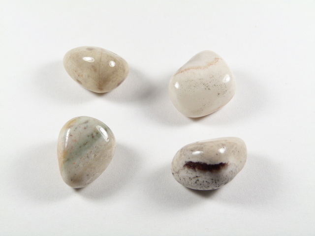 Sardoniks/ sardonyks - kamień gładzony, polerowany, szlifowany i bębnowany w formie otoczaka. Kamień sardoniks w formie naturalnych, gładzonych, jasnych kamyczków. Cztery gładkie, jasne kamienie leżące na białym tle.