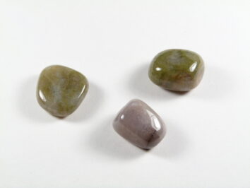 Sardoniks/ sardonyks - kamień gładzony, polerowany, szlifowany i bębnowany w formie otoczaka. Sardoniks właściwości kamień gładzony. Trzy wypolerowane kamienie leżą na białym tle.