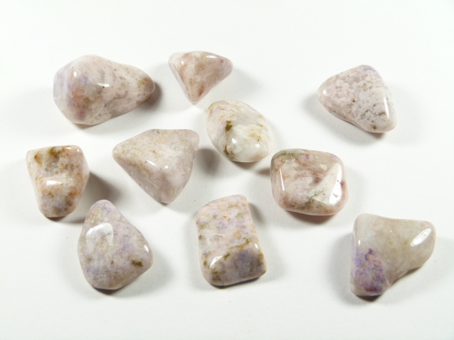 Tanzanit preria kamień w formie naturalnych, pastelowych kamieni gładzonych. Dziesięć gładkich, jasno-fioletowych kamieni leży na białym tle.
