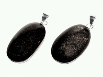 Wisiorek ze srebrnego obsydianu, dwa egzemplarze na jasnym tle. Dwa owalne czarne wisiorki z połyskującymi drobinkami i srebrnymi uchwytami na białym tle.