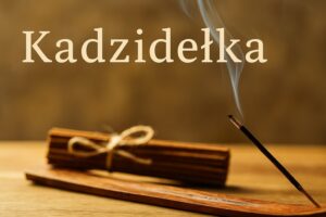Kadzidełka do czego służą – zapalone kadzidło na drewnianej podstawce z unoszącym się dymem. Płonące kadzidełko na drewnianej podstawce, w tle związane patyczki kadzideł.